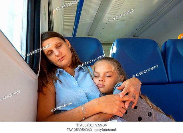 Mom and daughter sleep in a seated carriage of an electric train