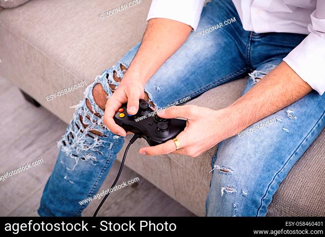 Happy, smiling, fun, entertainment, hands close up, details. Closeup of young hipster man sitting on couch at home, playing video game on laptop computer while...
