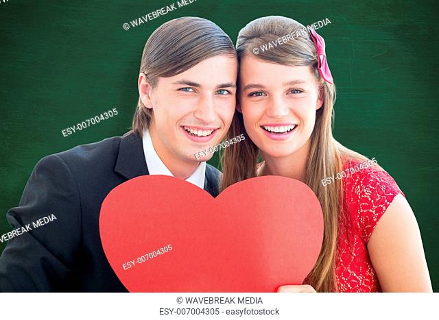 Composite image of cute geeky couple smiling and holding heart