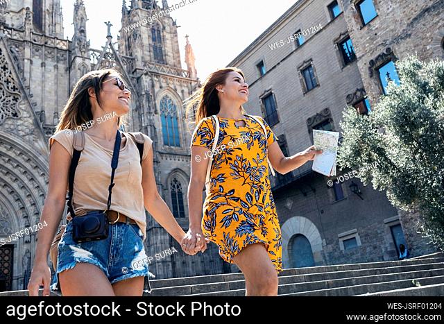 Female friends holding hands while walking against Barcelona Cathedral Square at Barcelona, Catalonia, Spain