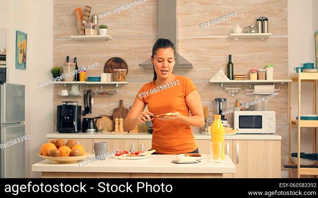 Cheerful woman in the morning dancing and spreading butter on roasted bread. Knife smearing soft butter on slice of bread