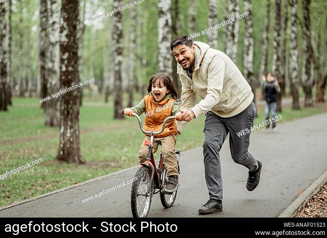 Father running by son learning bicycle on footpath at park