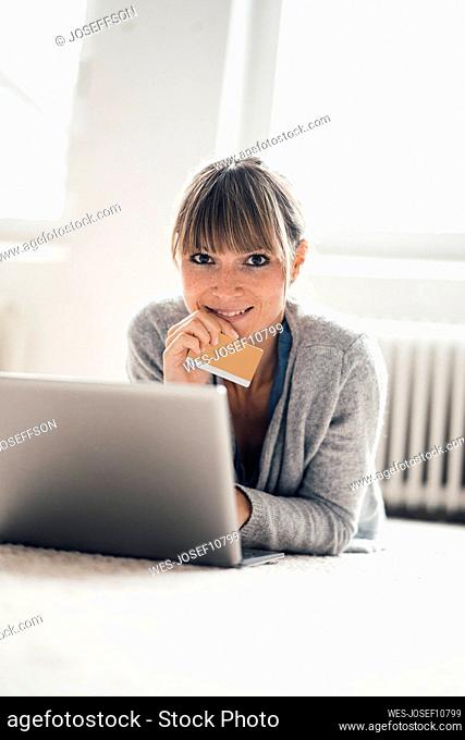 Smiling woman with credit card using laptop at home