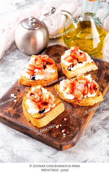 Bruschetta with tomatoes, mascarpone cheese and balsamic sauce on wooden cutting board on light background