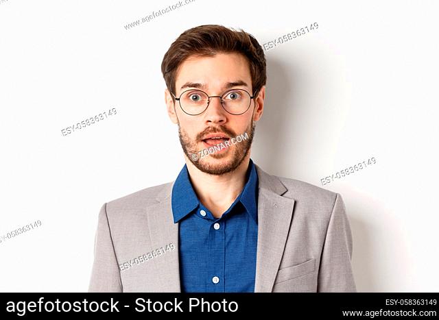 Close-up of surprised business man in glasses and suit gasping amazed, hear good news, standing on white background