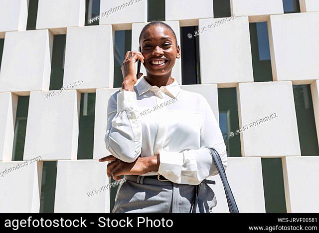 Smiling professional talking on mobile phone while standing in front of block shape wall