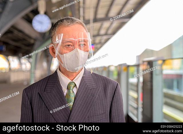 Portrait of mature Japanese businessman with mask and face shield for protection from corona virus outbreak at skytrain station