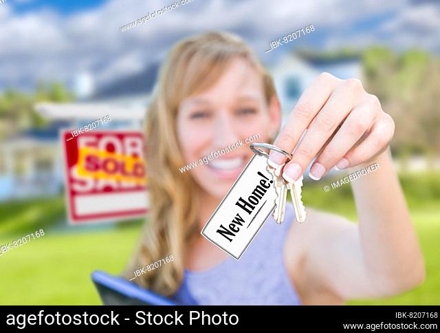 Woman holding new house keys with new home card in front of sold real estate sign and home