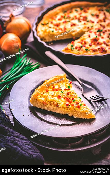 Piece of homemade onion tart or pie with bacon and chive on wooden background