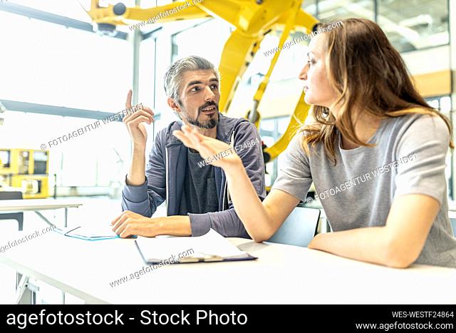 Technician and engineer sitting in factory discussing work solutions