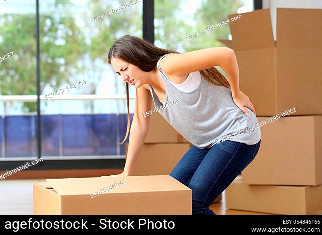 Woman in pain moving boxes suffering backache grabbinng lumbar area at home