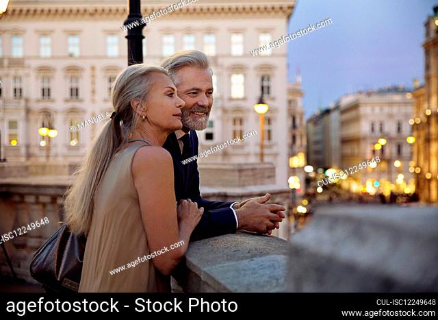 A couple leaning against a balustrade overlooking Vienna during the evening