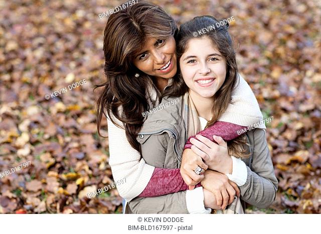 Hispanic mother and daughter hugging in autumn leaves