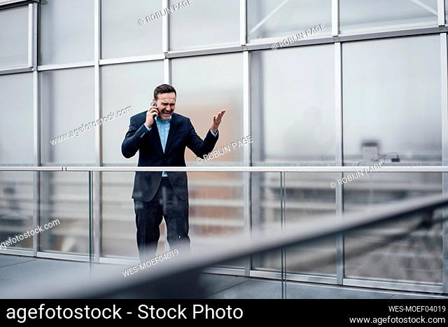 Frustrated businessman arguing on smart phone standing on balcony