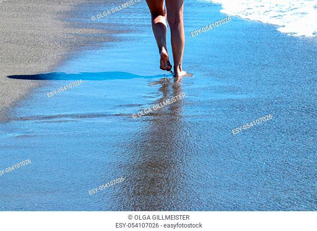 Woman walking on beach. Woman walking with healthy tanned female feet on wet sea sand on a bright summer day. The girl leaving footprints in the sand