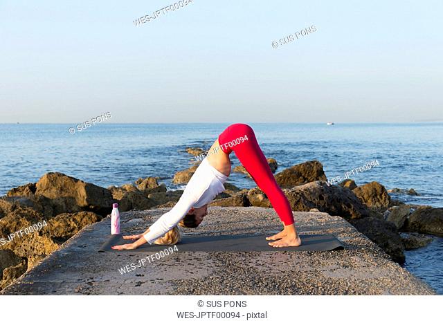 Young woman practicing yoga on the beach, doing downward facing dog