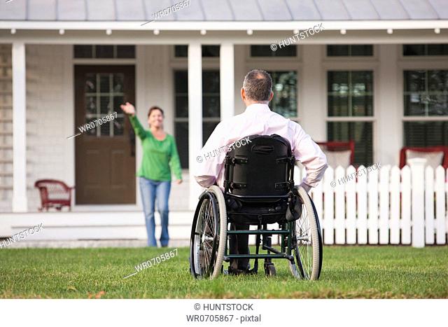 Woman waving from their home to her husband in a wheelchair with a spinal cord injury
