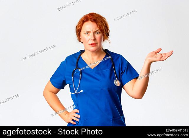 Medicine, healthcare and coronavirus concept. Frustrated and annoyed redhead female medical worker, doctor looking confused and angry
