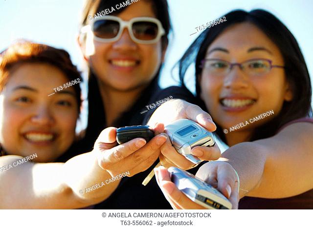 3 asian women holding cell phones out in hands