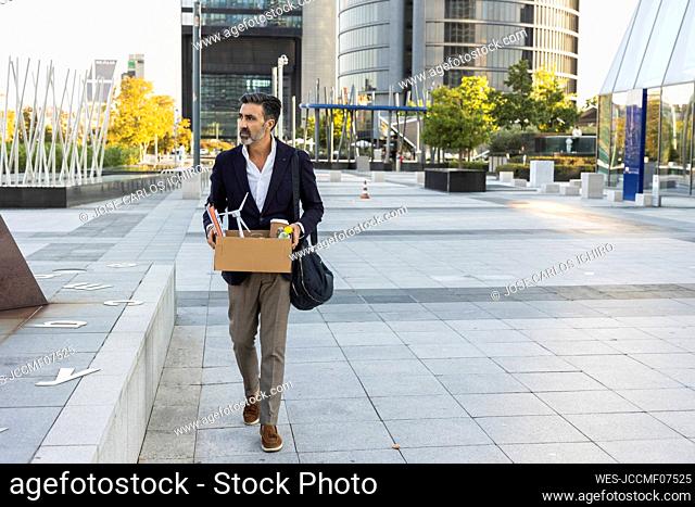 Businessman holding box walking in front of office building