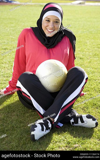Muslim teenager sitting on ground with soccer ball