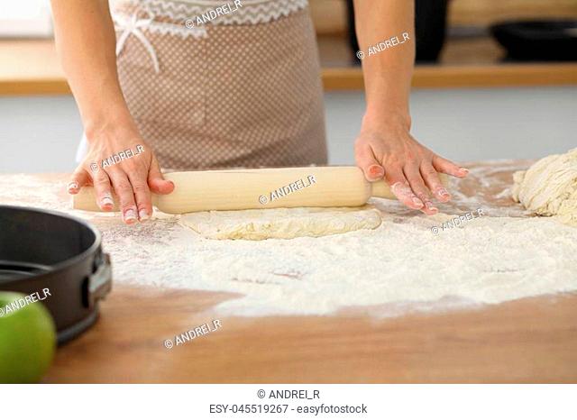 Female hands making dough for pizza or bread while using rolling pin. Baking concept