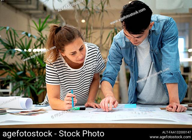 Front view of architects leaning on table while working on blueprints