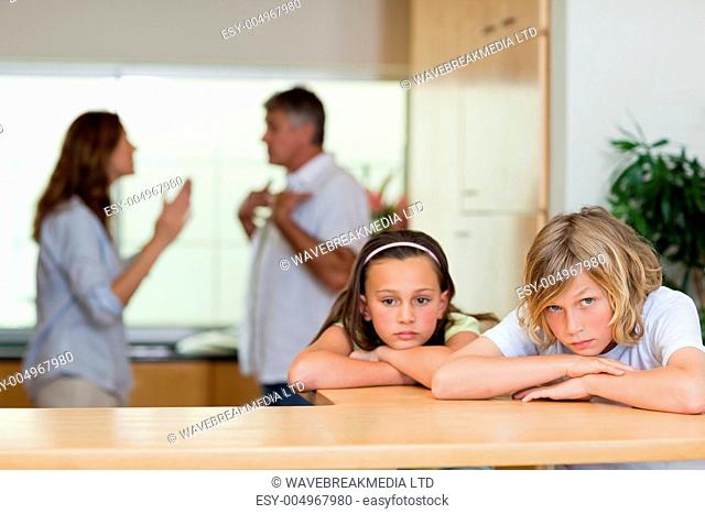 Sad looking siblings with arguing parents behind them