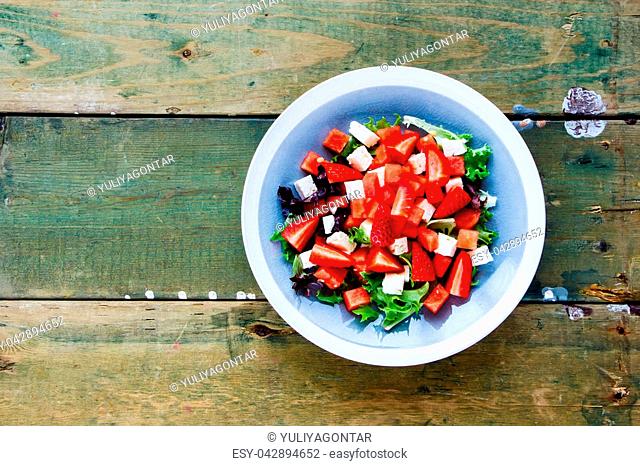 Summer watermelon salad with arugula, feta cheese and fresh strawberry on wooden background. Flat lay, top view