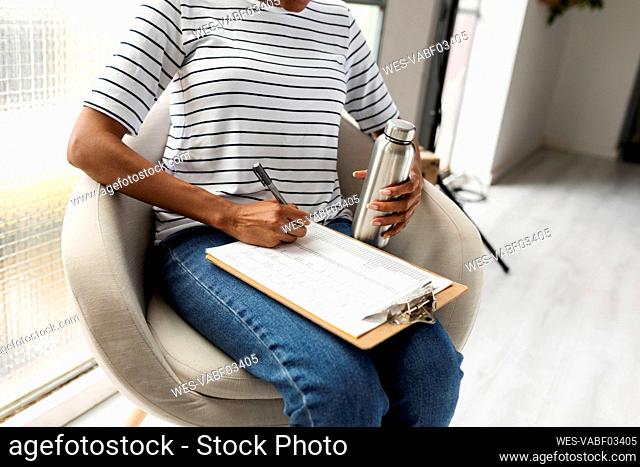 Woman sitting in chair at casual office, writing on clipboard