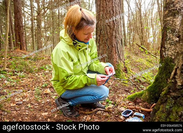 A woman geocaching. Women in woods find geocache container near tree