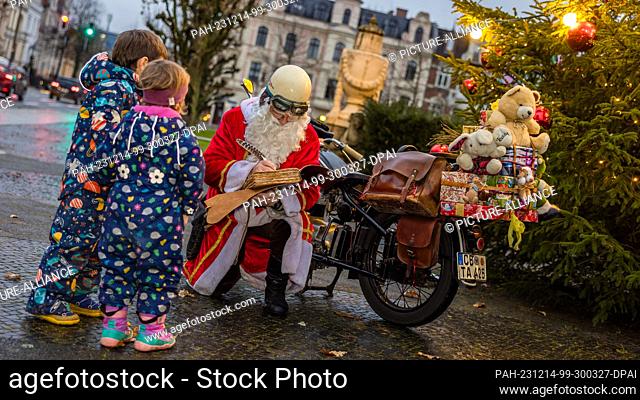 14 December 2023, Brandenburg, Cottbus: A man dressed as Santa Claus writes down children's wishes in his ""wish book"" while kneeling in front of his...