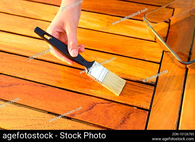 hand holding a brush applying varnish paint on a wooden garden table - painting and wood maintenance oil-wax