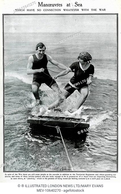 A couple water-planing (or planking) on a wooden raft -- the photograph has been taken from the motor boat which is towing them