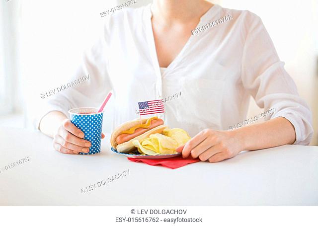 independence day, celebration, patriotism and holidays concept - close up of woman eating hot dog with american flag decoration and potato chips
