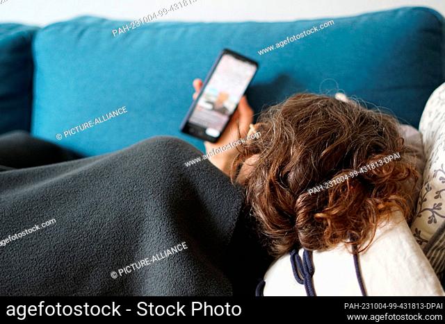 ILLUSTRATION - 28 September 2023, Berlin: A woman lies on a sofa covered with a blanket and watches a video on the social media platform Instagram on her cell...