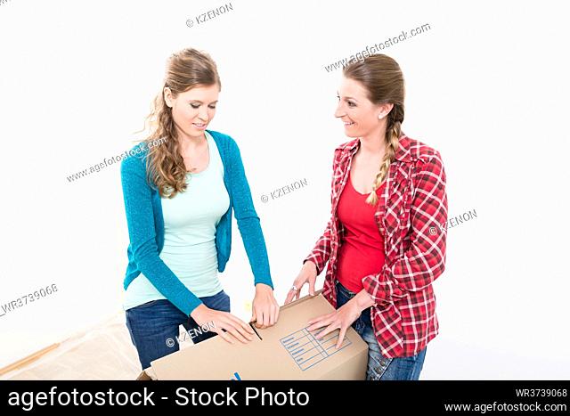 Close-up of smiling young women packing the cardboard box against white background
