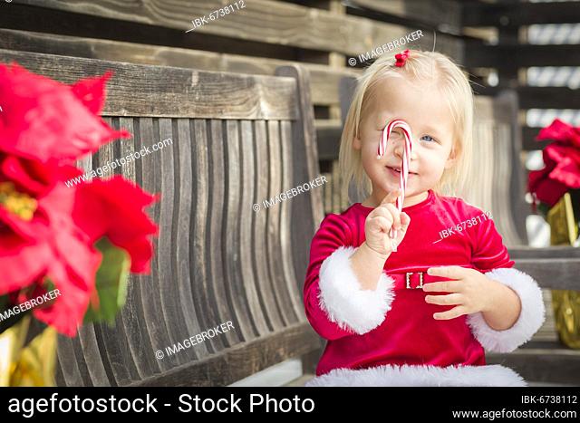 Adorable little girl sitting on A bench with her candy cane outside