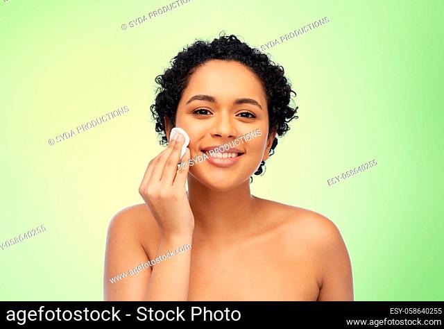 happy african woman cleaning face with cotton pad