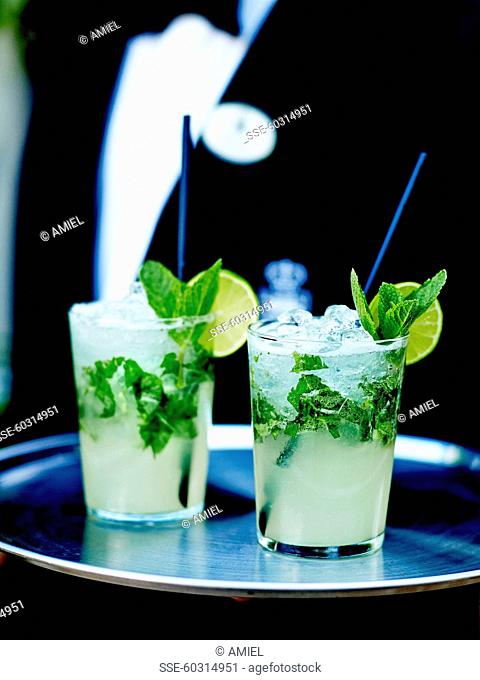 Waiter carrying a tray with two glasses of vodka mojito