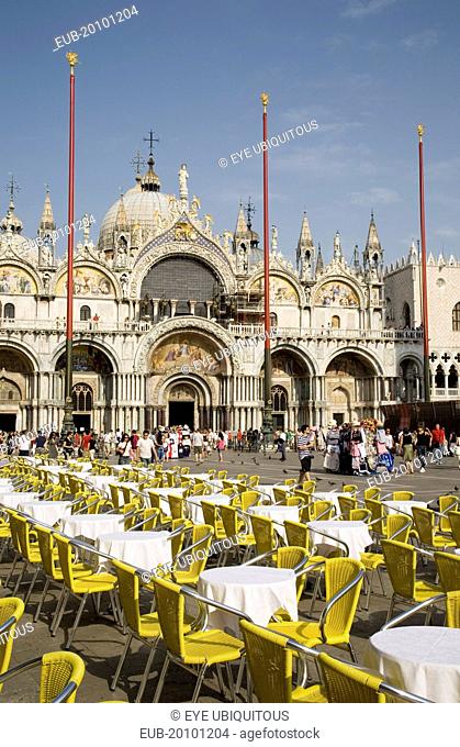 Centro Storico St. Marks Square Cafe tables prepared for customers in early morning sunshine with facade of Basilica di San Marco behind