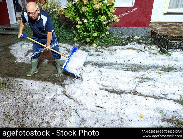 09 September 2022, Mecklenburg-Western Pomerania, Stralsund: A man shovels hailstones from the sidewalk with a snow shovel