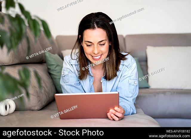 Smiling woman using tablet while relaxing on sofa at home