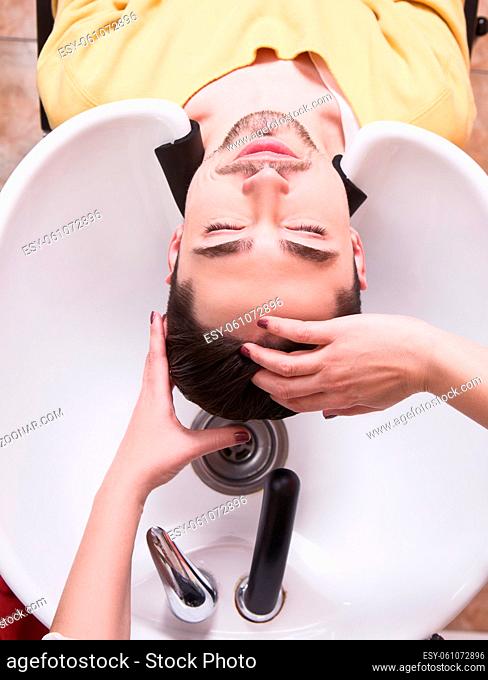 Topview picture of young man lying with his eyes closed in beauty saloon. Handsome man having his hair washed in hairdressing saloon