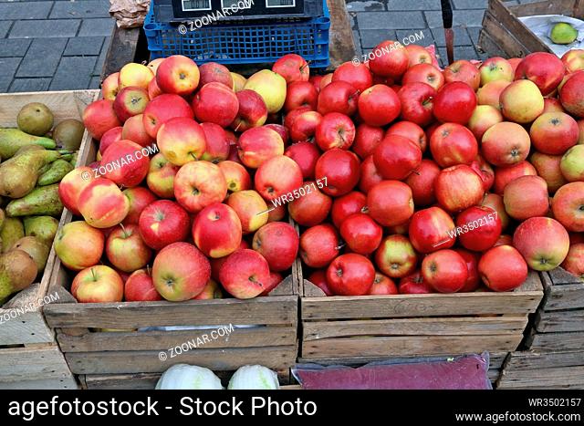 Street market of fresh red garden apples fruits in wooden boxes. Cloudy March day outdoor sity shot