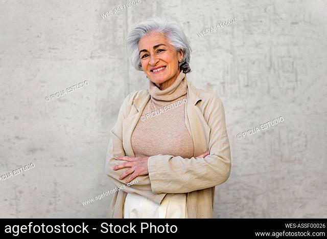 Smiling woman with arms crossed standing in front of wall