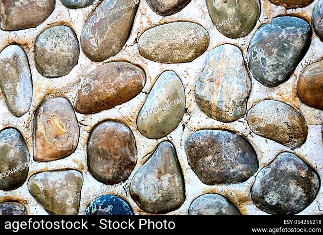 A fragment of stone wall decorated with sea pebbles of different shapes and sizes. Background image