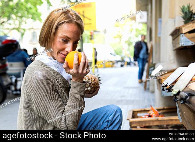 Woman smelling fruit while crouching at street market