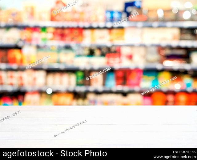 White wooden board empty table in front of blurred background. Perspective white wood board over blurred colorful supermarket products on shelvest - mockup for...