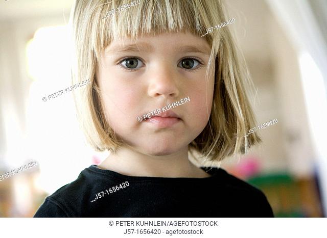 Portrait of a 4 year old girl in a black shirt with blond straight hair looking engagingly into the camera